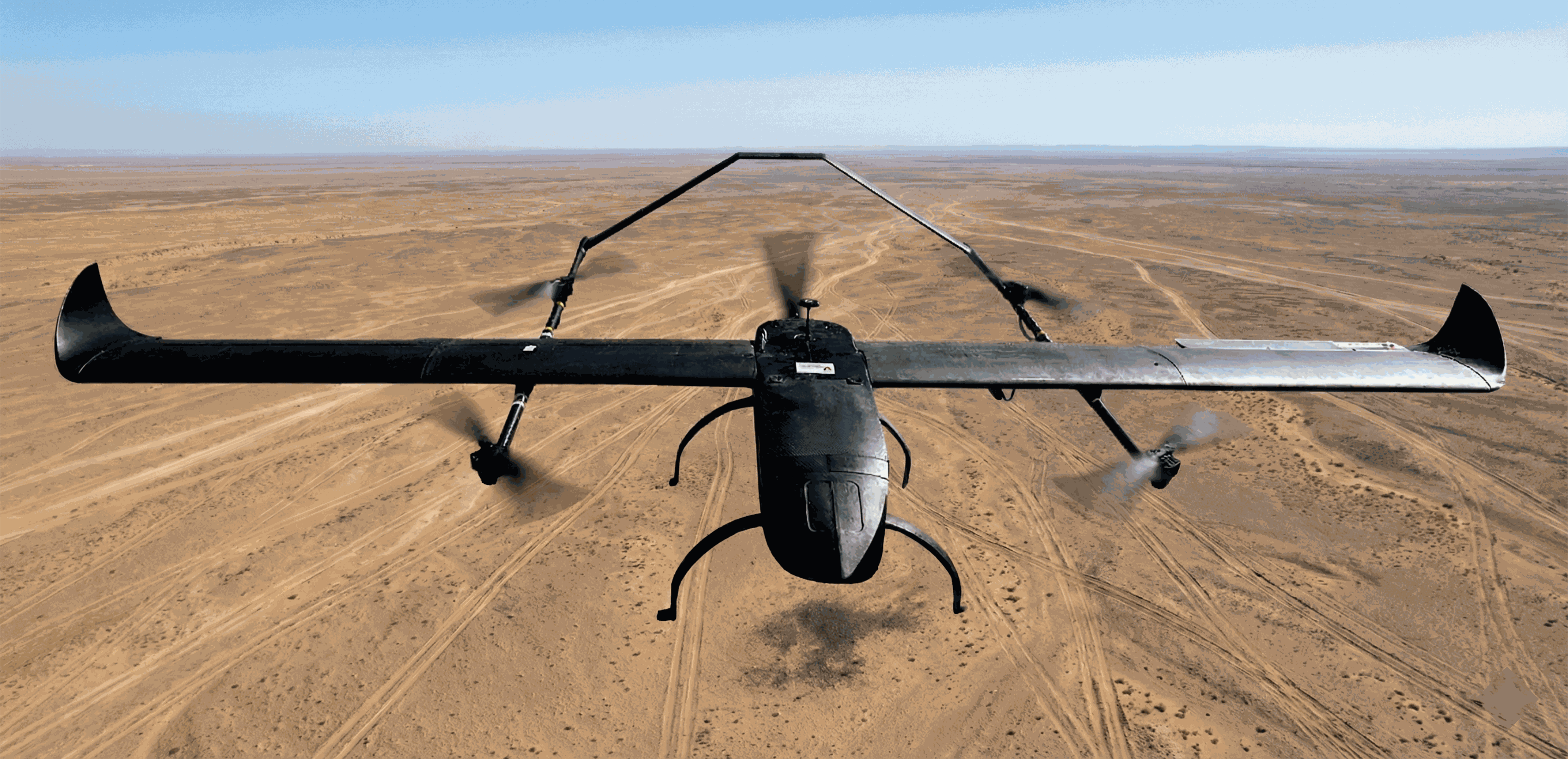 Hans Hybrid VTOL fixed-wing drone conducting a long-range aerial survey mission over arid terrain. The image showcases the UAV's carbon composite airframe and hybrid propulsion system in flight, demonstrating stability for mapping and surveillance.